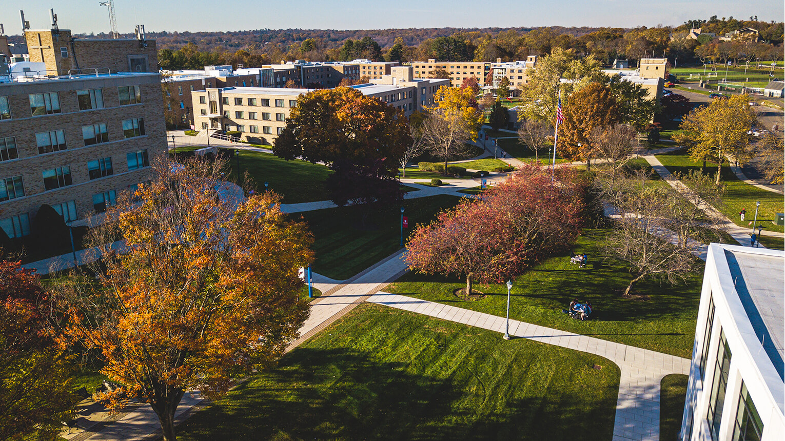A scenic view of a Fairfield University campus featuring several buildings, including Canisius Hall, surrounded by lush green trees.  