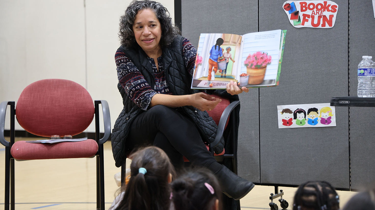 Volunteer reading a colorful book aloud to a group of children.