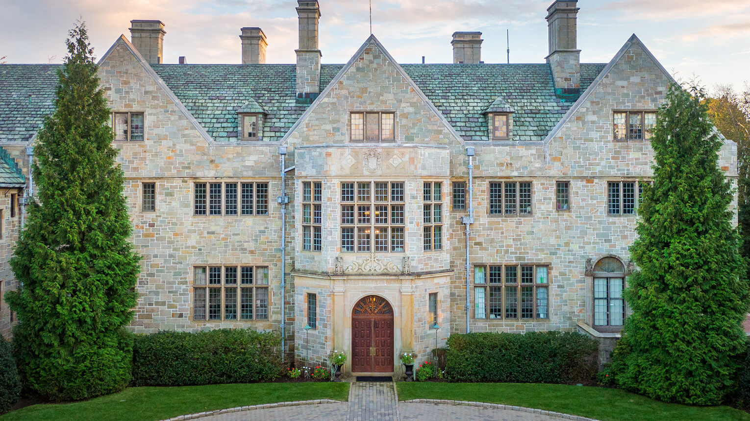 Bellarmine Hall building with a steep green roof and symmetrical design. Tall trees flank the entrance, conveying elegance and grandeur.