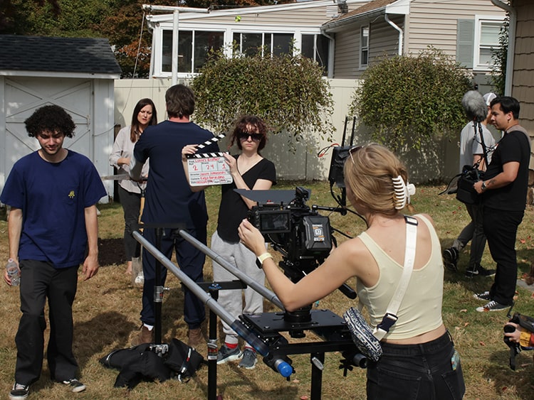 Behind-the-scenes shot of students on the set of a student-produced, student-written film, located outside in a residential backyard.