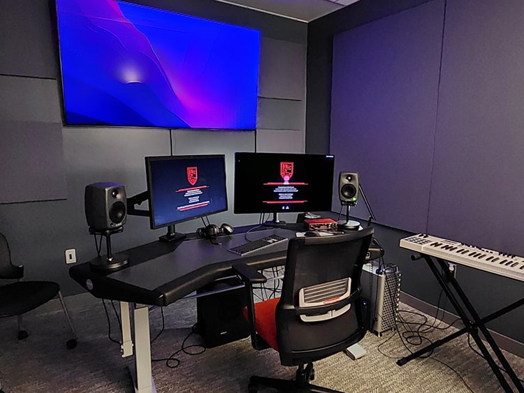 Dual-monitor desk setup in a soundproof studio, equipped with speakers, a TV monitor, and a electric piano keyboard.
