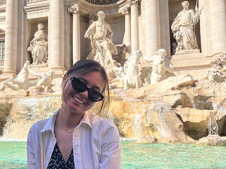 Fairfield student smiling while standing in front of the Trevi Fountain on a sunny day.