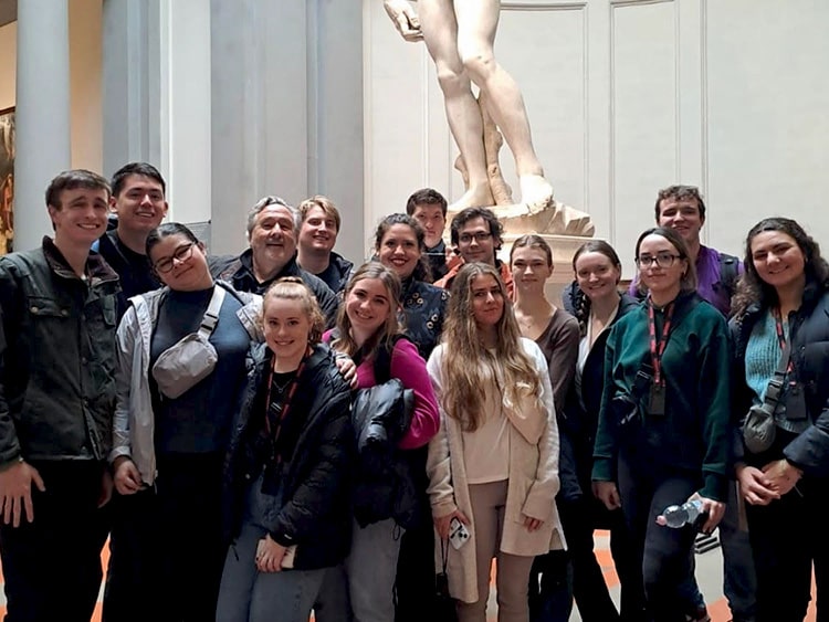 Fairfield students posing in a tour group underneath the famous marble Statue of David in Florence, Italy.