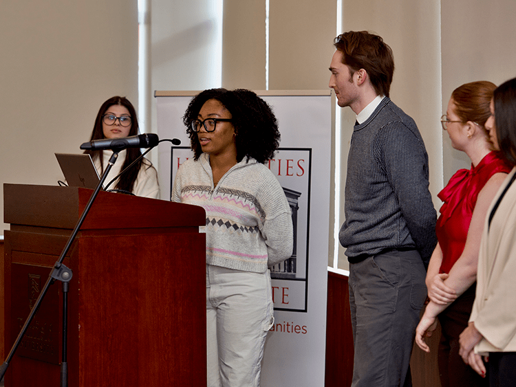 Students speaking at a Fairfield-branded podium as they present their collaborative student-faculty research.
