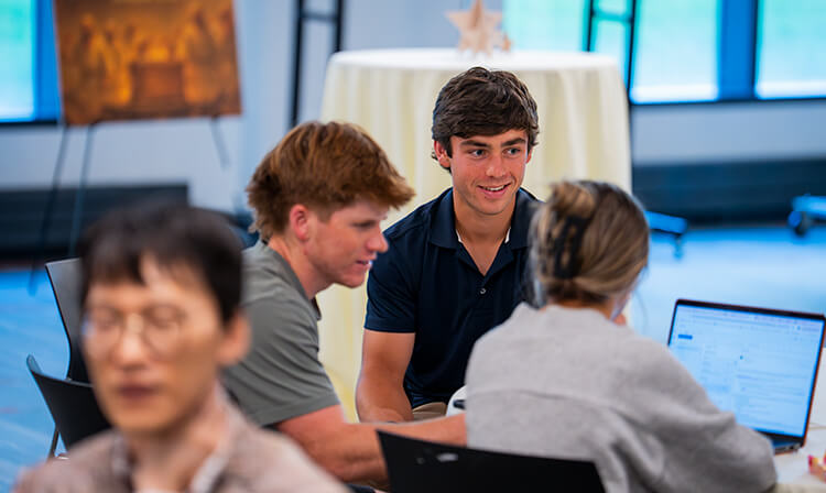 Students engaged in discussion around a table in a conference room, focused on collaborative work.  