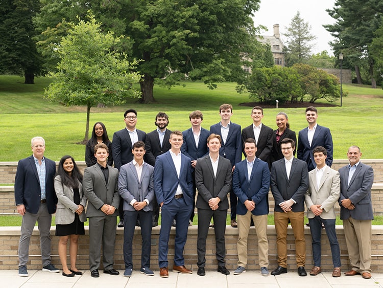 Group of business students and two advisors standing on the outdoor steps to the Dolan building.