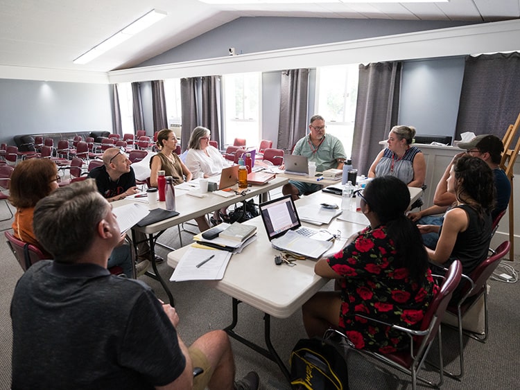 Creative writing MFA candidates engaging in a group discussion in a classroom during a writing workshop.