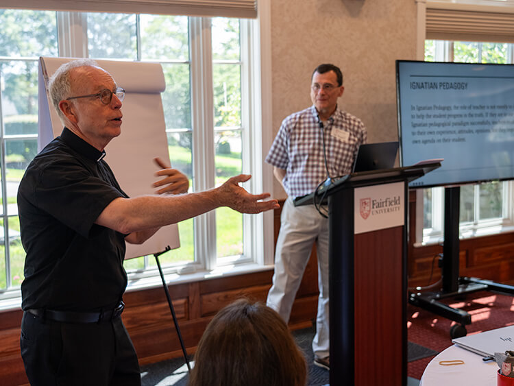 A man presenting to an audience, engaging with a group of attentive listeners in a conference setting.