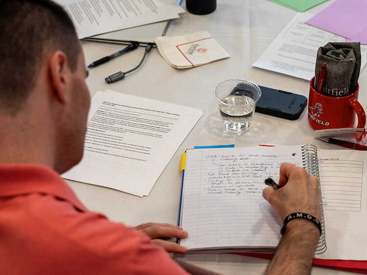 A man focused on writing in a notebook, with a pen in hand and a thoughtful expression on his face.