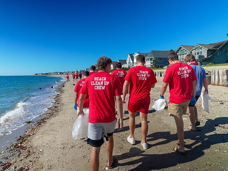 Fairfield students walking on the shoreline, sporting their 'beach clean-up crew' uniform shirts as they clear the beach of trash.