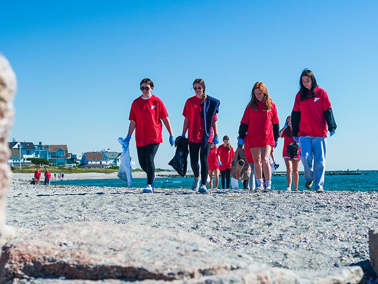 Fairfield students in red surveying a beautiful sandy beach as they inspect it for trash for removal.