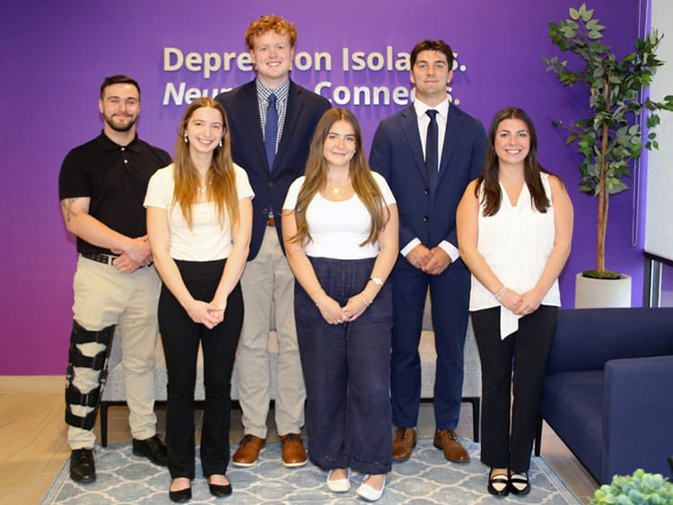 Fairfield Meditz students standing in front of a "Depression Isolates. NeuroStar Connects." wall text while visiting Neuronetics.