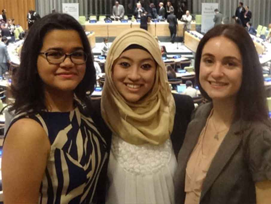 Three women smiling together for a photo at a United Nations conference, showcasing unity and cultural representation.