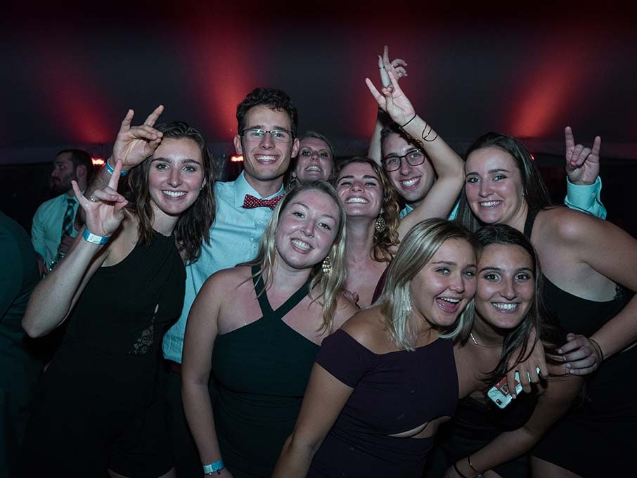 A group of students smile holding up their hands in a stag shape.