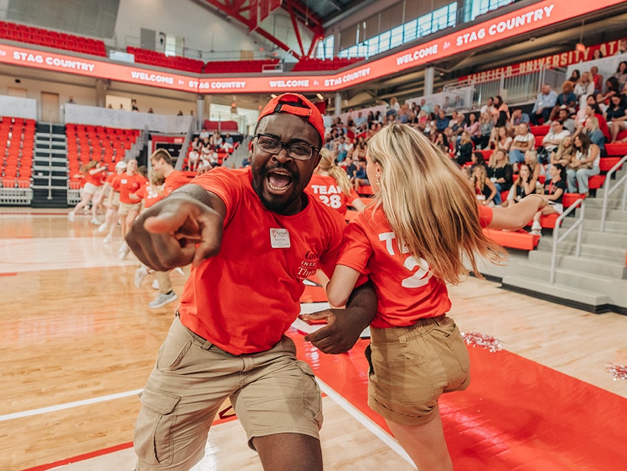 Orientation leaders swinging and dancing, arm-in-arm, as they hype up the crowd in the Mahoney Arena.