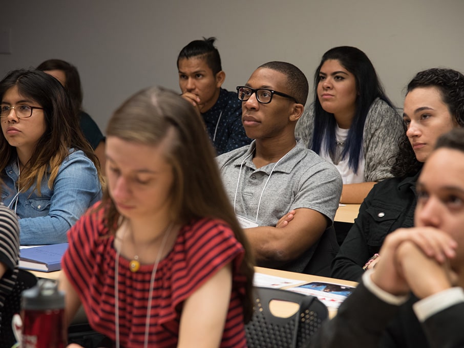 Students sitting in a classroom and listening intently while taking notes for a lecture.