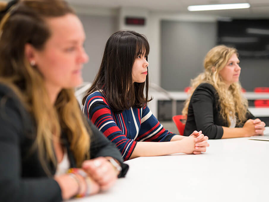 Three female students at a table in a college classroom, collaborating and sharing ideas during a discussion.