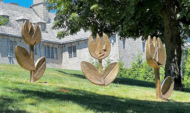 Three flower sculptures displayed in front of a house, showcasing vibrant colors and intricate designs.  