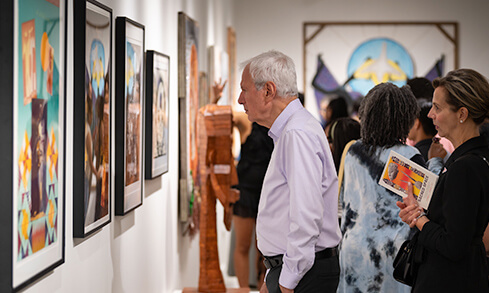 Visitors admiring art pieces in an art gallery, engaged in conversation about the exhibits.