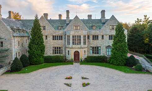 Bellarmine Hall with gabled roof, chimneys, and formal gardens surrounding a quiet circular courtyard in soft evening light.