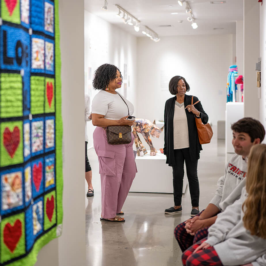 A group of people stands in front of an art display, engaging with the artwork and each other