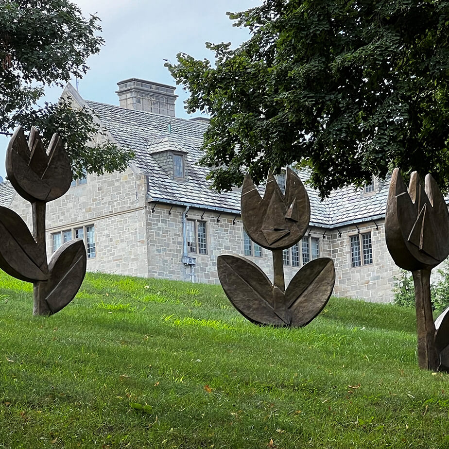 Three flower sculptures stand on a grassy hill, showcasing intricate designs against a natural backdrop.  