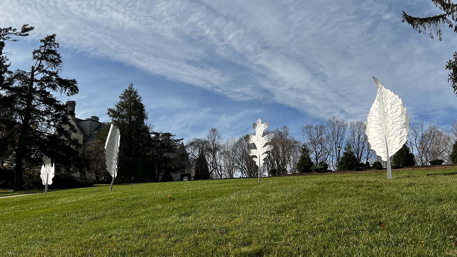 Several white sculptures are arranged on a lush green hill, creating a striking contrast against the vibrant grass.