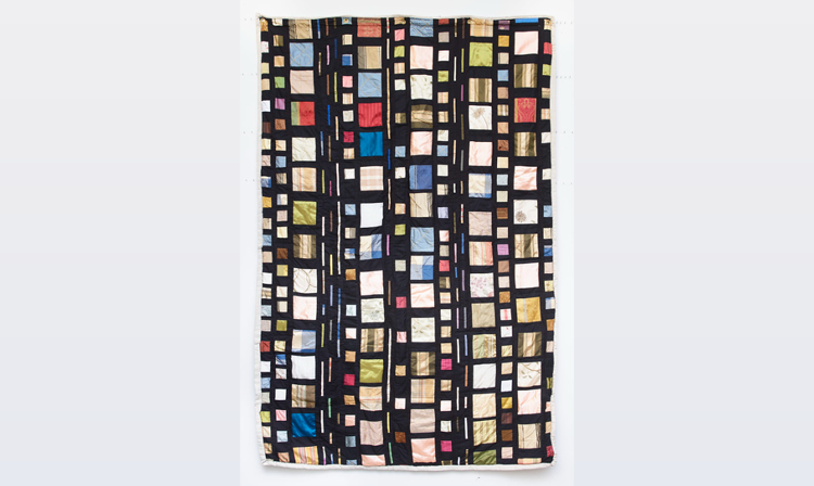 Quilt over a grey background. The quilt features several brightly colored squares and rectangles over a black base