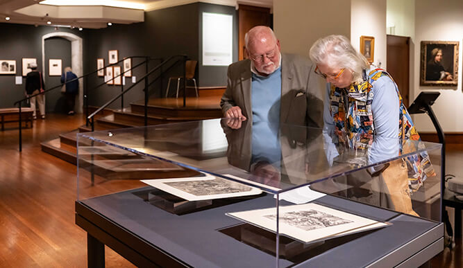 Two individuals observing artwork in the Bellarmine Gallery, engaged in discussion about the pieces on display.  