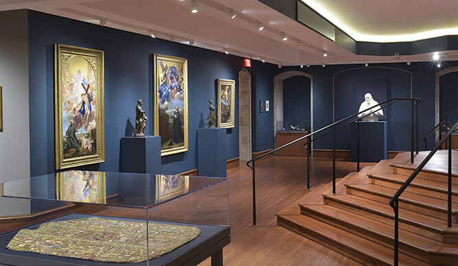 Interior view of Bellarmine Hall Galleries with blue walls and a staircase in the background.