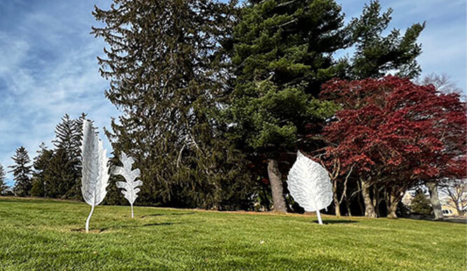 Three silver metal leaves resting on green grass, creating a contrast between the metallic and natural elements.