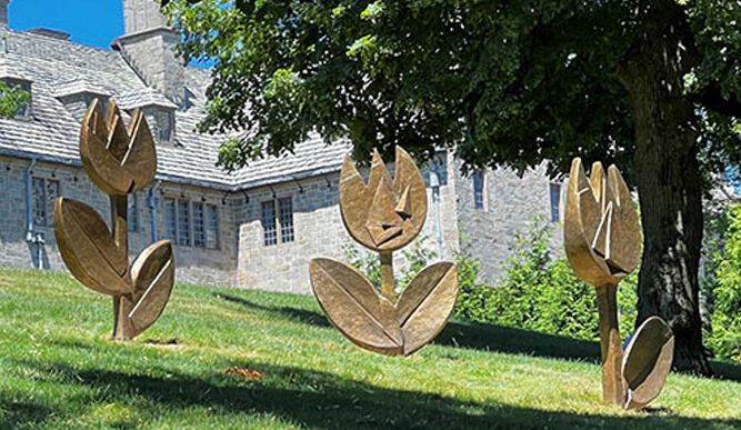 Three flower sculptures displayed in front of a house, showcasing vibrant colors and intricate designs.