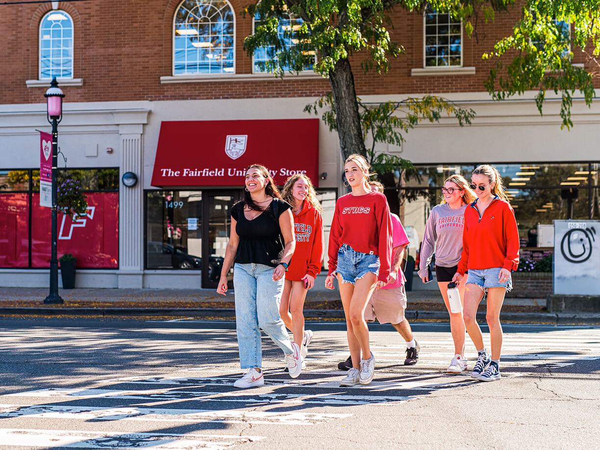 Several young women crossing a street in front of Fairfield University Bookstore, laughing and chatting as they navigate the urban environment together.