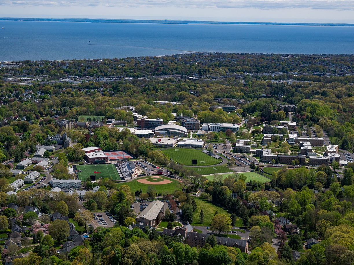 Aerial view of the entirety of Fairfield's sprawling, green campus with the Long Island Sound in the background.