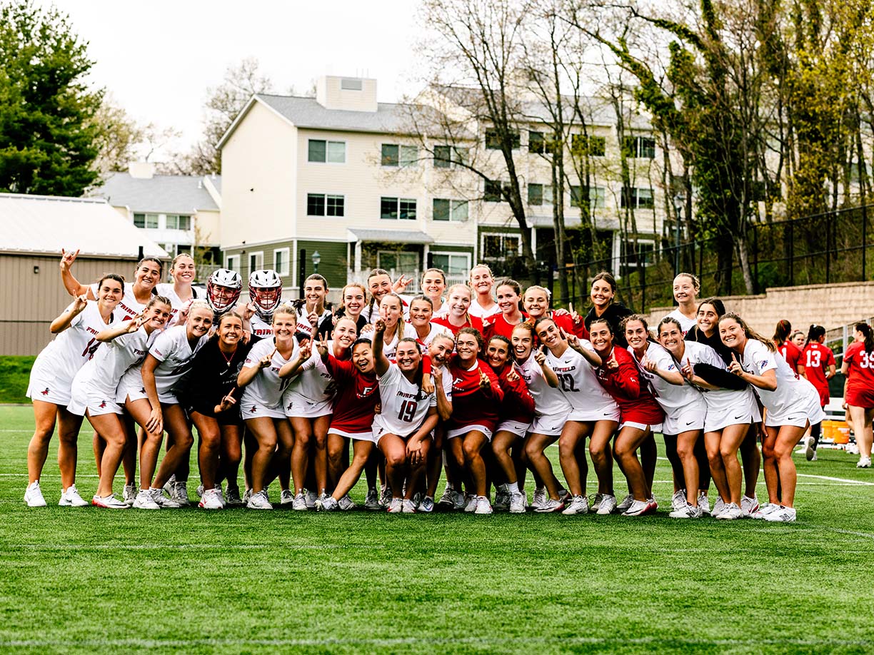 Women's lacrosse team smiles together for a group photo on the field, showcasing their team spirit and unity.