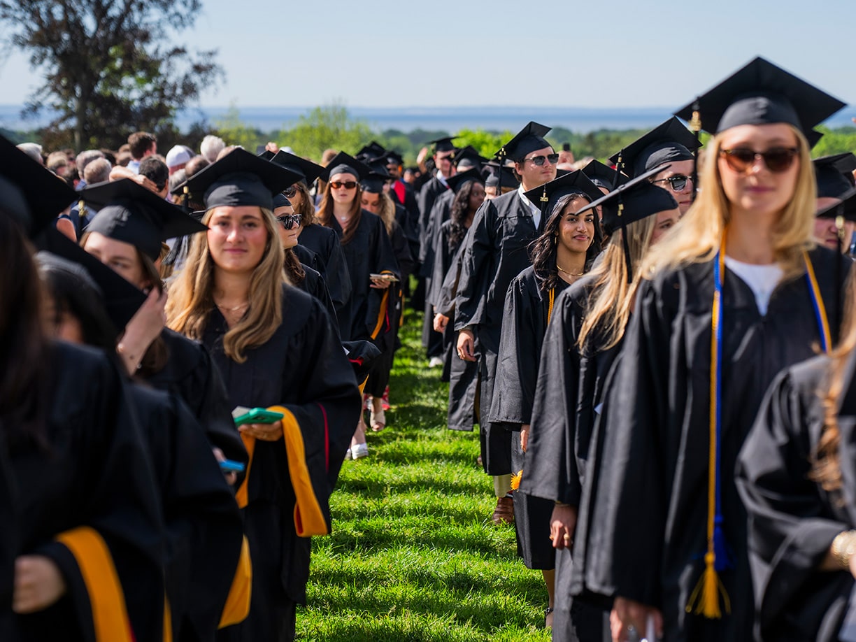Undergraduate students in caps and gowns processing down Bellarmine Lawn for Fairfield's 75th Commencement ceremony.