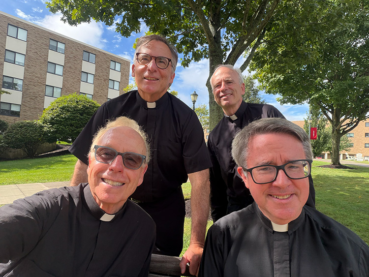 Four in-residence Jesuits taking a selfie outside on Fairfield's beautiful, lush campus during a break from blessing residence halls during move-in.