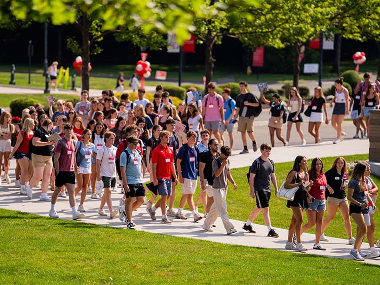 A large group of students walking together on a sidewalk, chatting and enjoying their time outdoors.