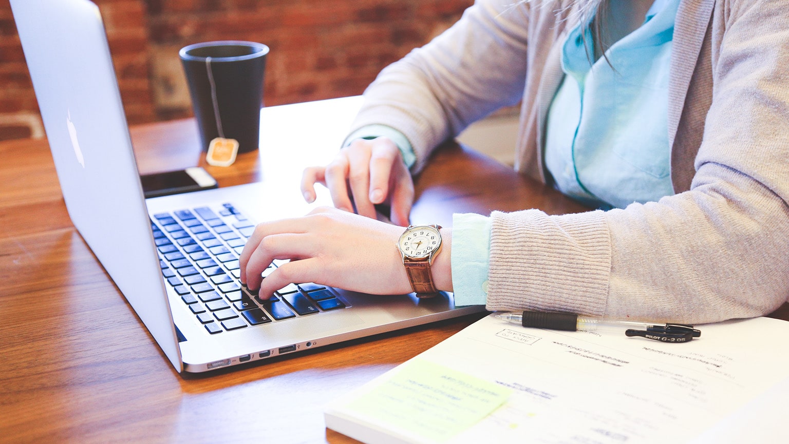 Professional employee typing an email on her laptop at her wooden, oak desk.