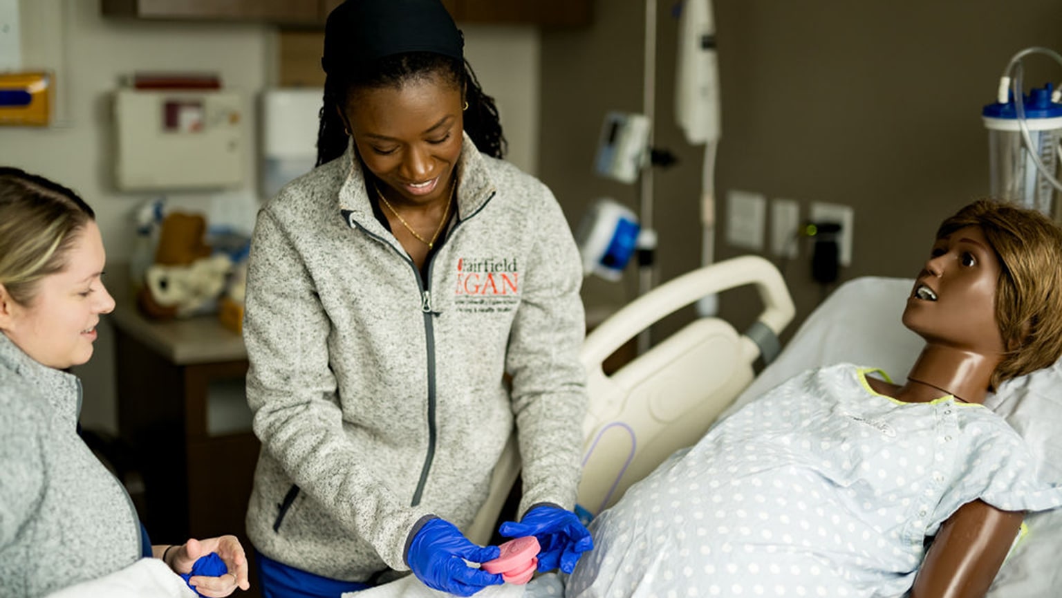 Two female nursing students simulating a midwifery scenario with a simulation doll.
