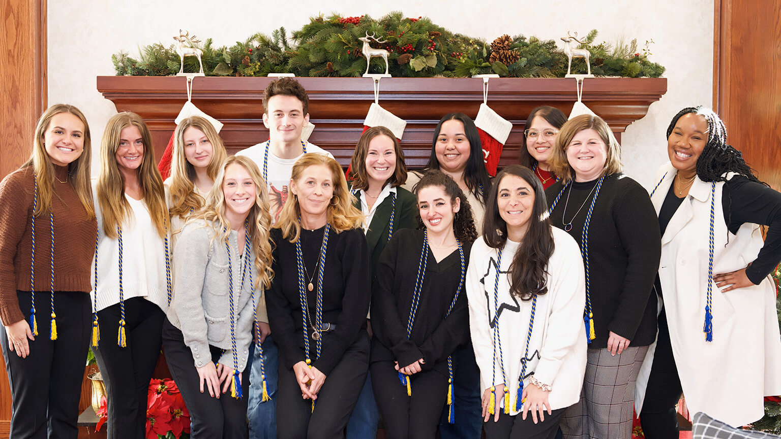 A cheerful gathering of students standing in front of a festive Christmas fire place, capturing a joyful moment in a photo.