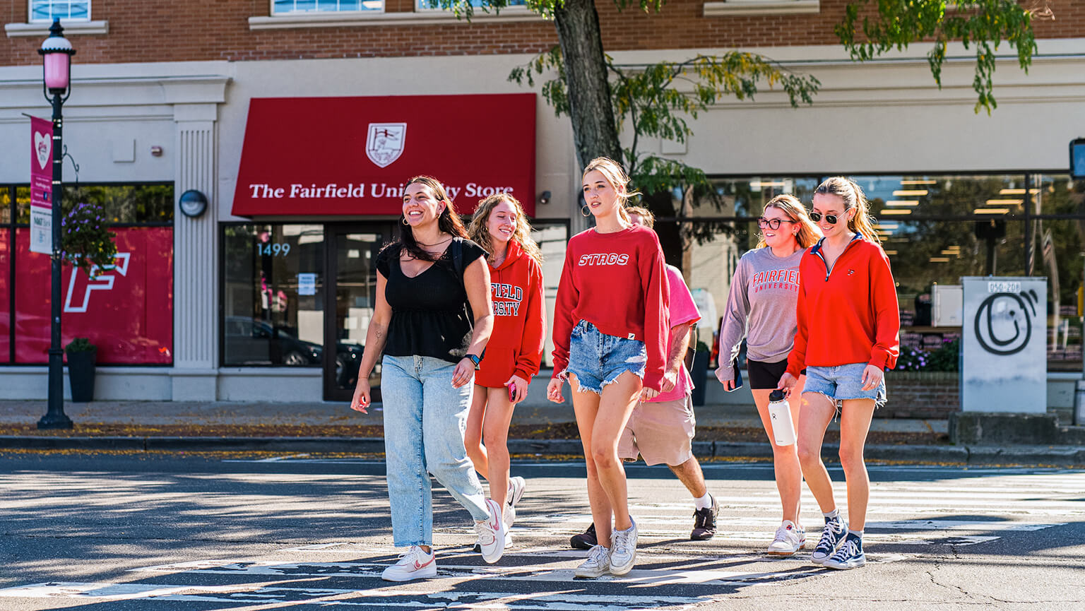 Several young women crossing a street in front of Fairfield University Bookstore, laughing and chatting as they navigate the urban environment together.  