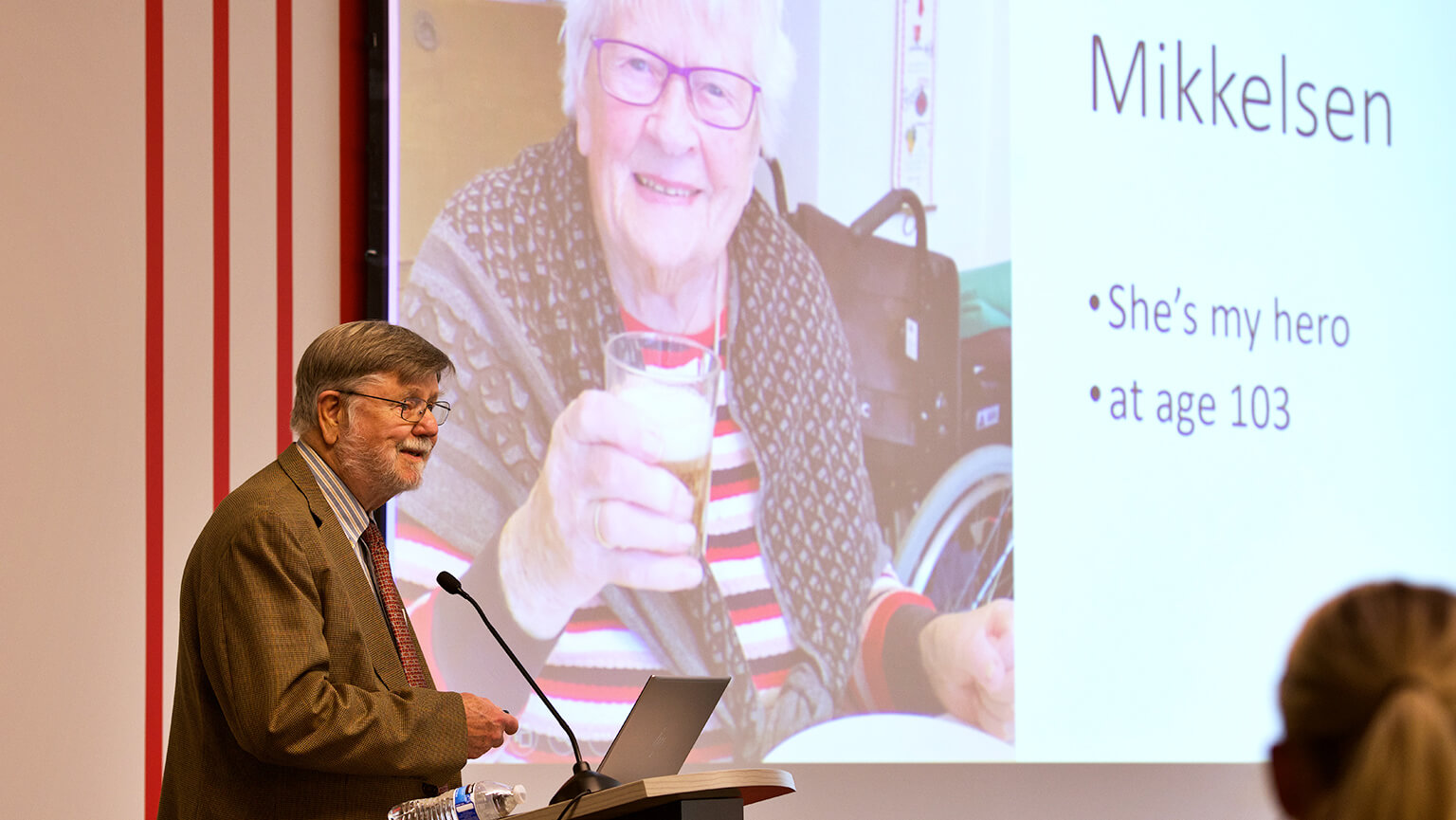 A man presenting information to an audience, using a projector and slides in a professional setting.