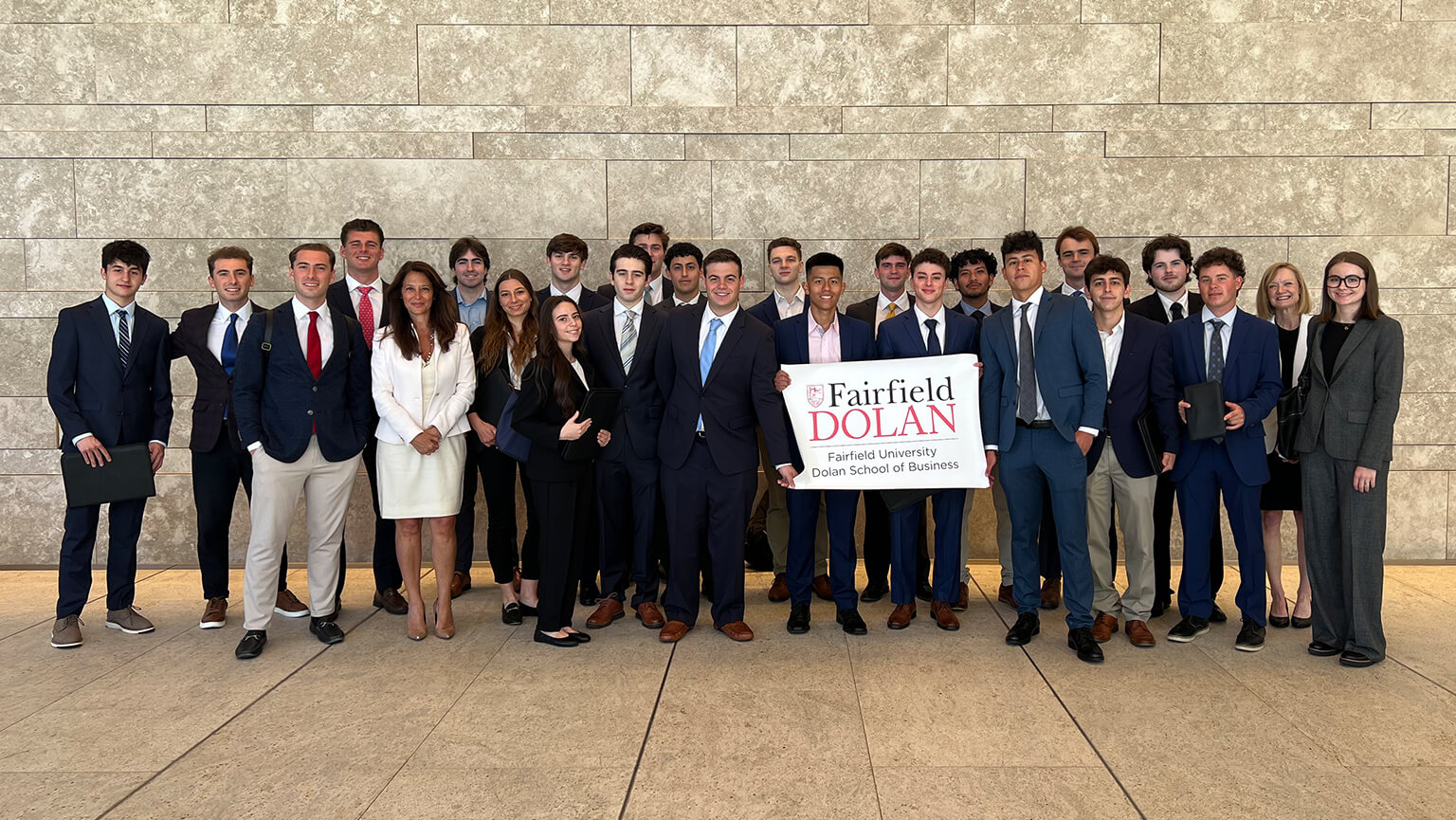 Several students in formal attire, including suits and ties, gather in front of a large office building.  