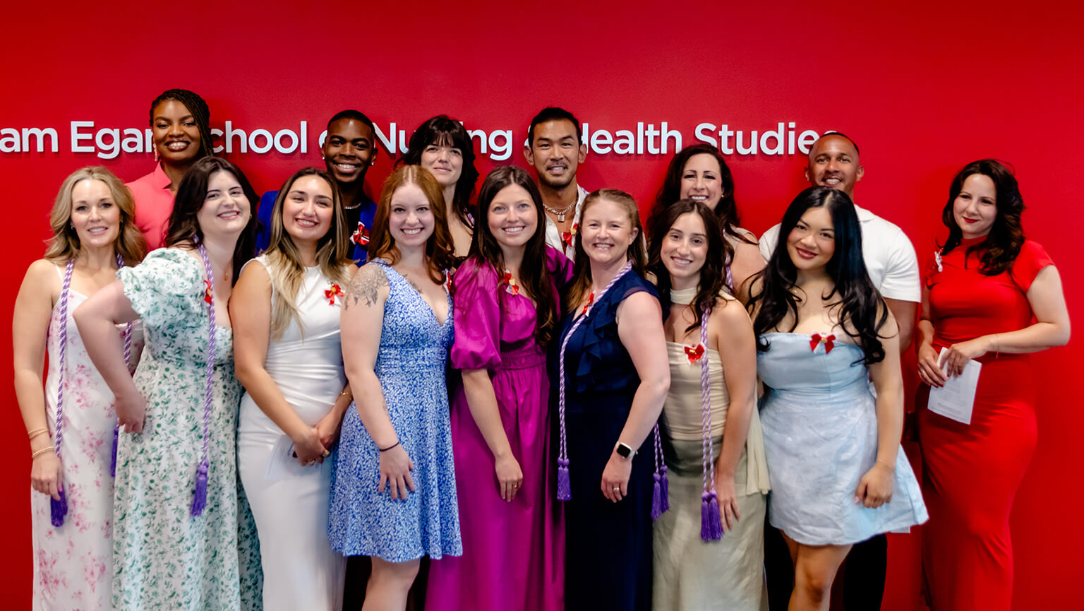 A group of second degree nursing students in colorful dresses and shirts smile and pose together for a photo indoors.. 