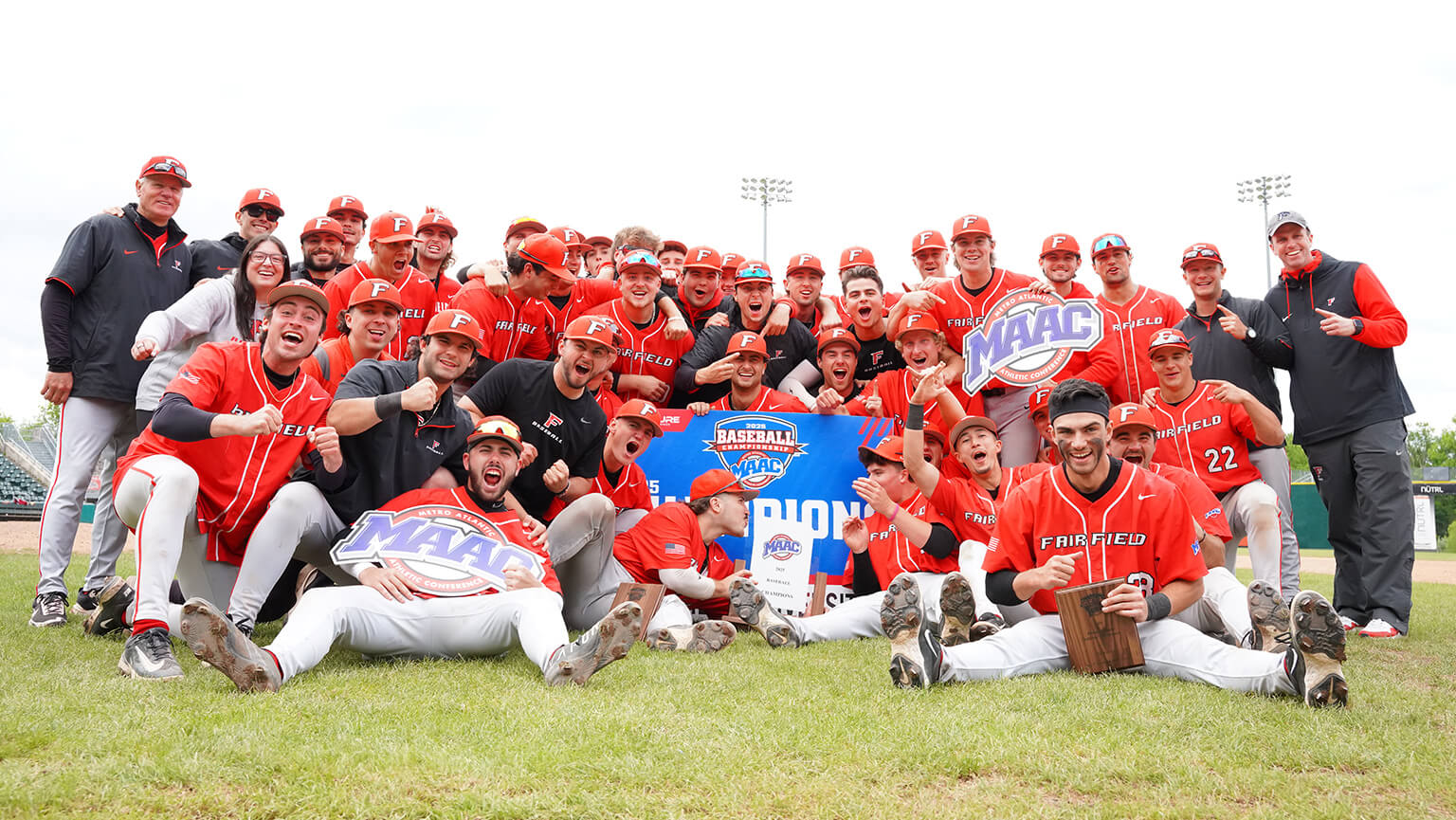 The Fairfield University baseball team stands together on the field, smiling for a group photo in their uniforms.
