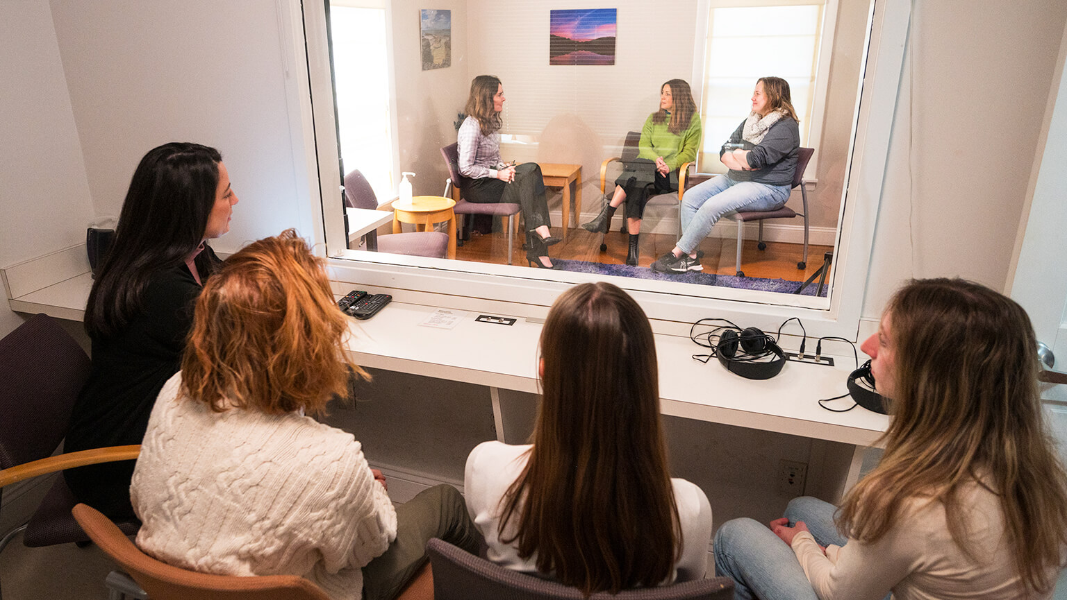 A group of women seated in a room, with a large window reflecting their engaged conversation and expressions.