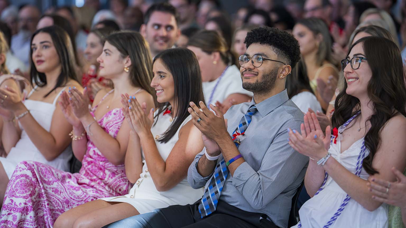 Image of a group of students seating, with one individual clapping in celebration.