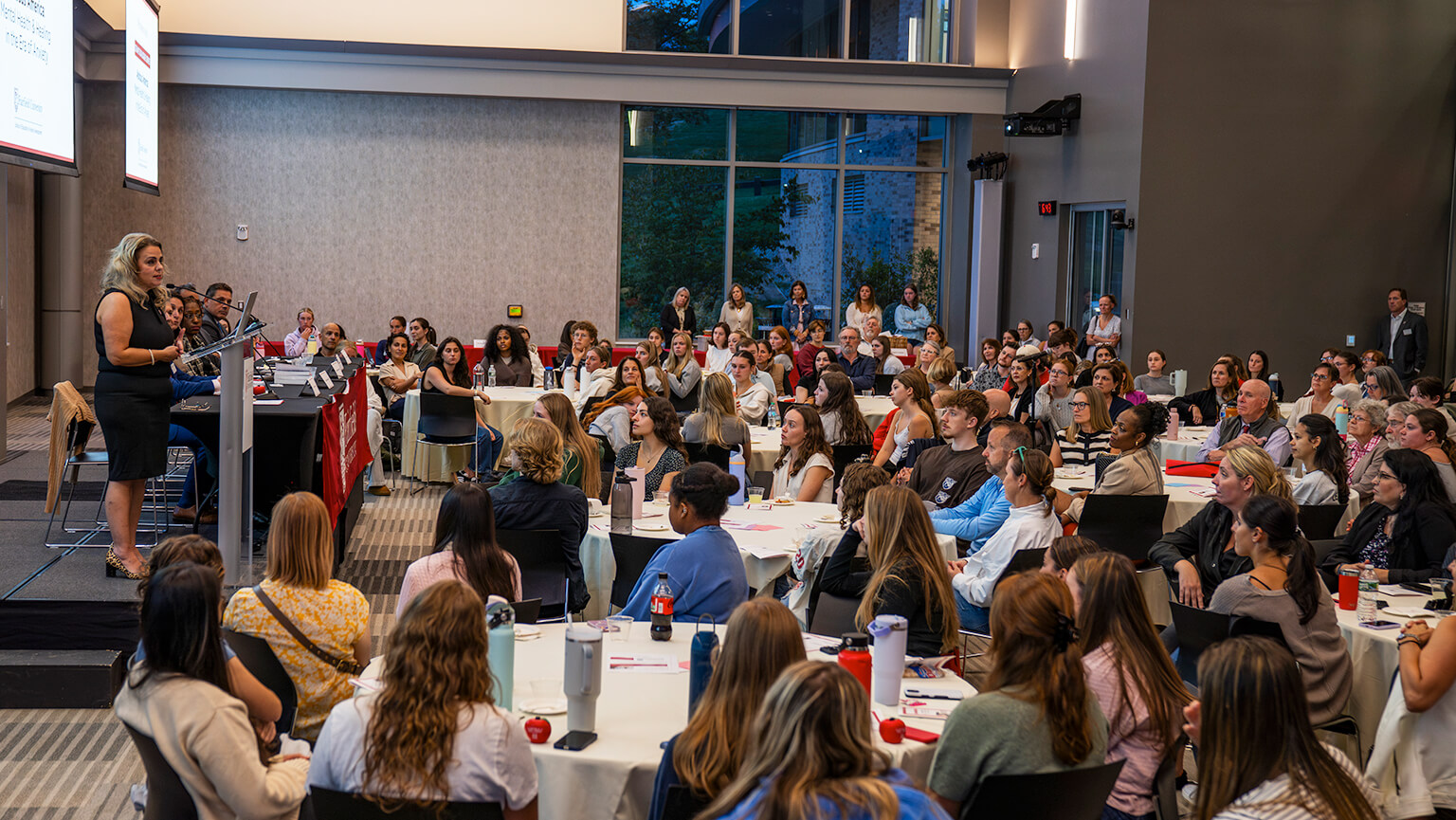 A woman presenting to a large audience, engaging the crowd with her speech and visual aids.