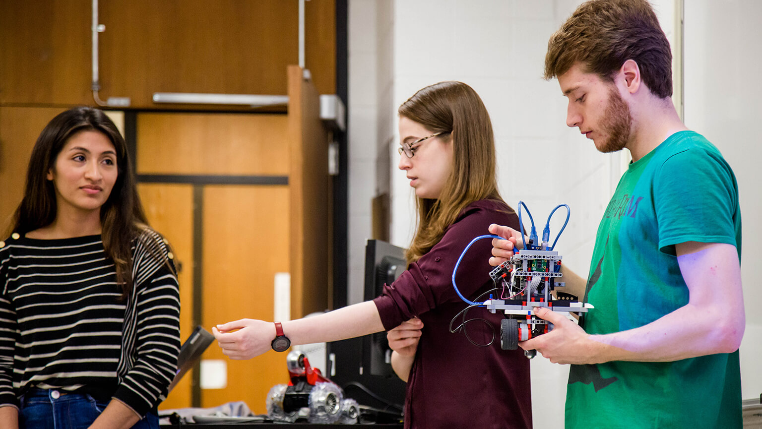 In a lab, students are focused on assembling a robot, using various tools and components for their project.